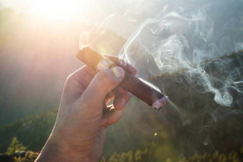 man holding a smoking cigar up in the air